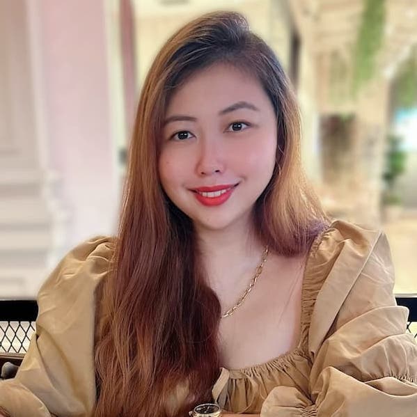 Asian woman with long hair and red lipstick and tan blouse slightly smiling