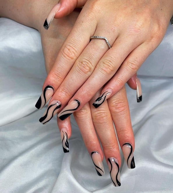 A woman's coffin fingernails with a nude nail polish base that has black swirls