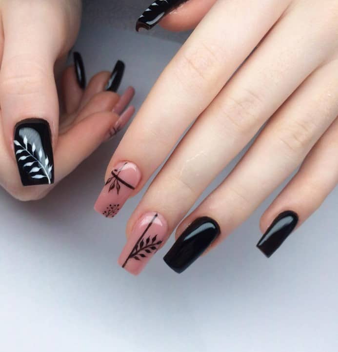 A closeup of a woman's fingernails with a black and nude manicure that has leaf art nail designs on select nails