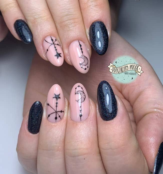 A closeup of a woman's fingernails with nude and black nail polish that has dangling moon and star nail art and glittery blue-black nails