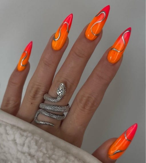 A woman's extra-long stiletto nails with red-and-orange ombre nails that has a lone silver swirl on each nail