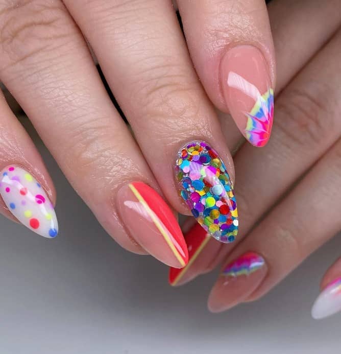 A closeup of a woman's long almond fingernails with a nude peach base featuring either vertical lines or tie-dyes that has multicolored chunky glitter and white nails adorned with playful multicolored polka dots