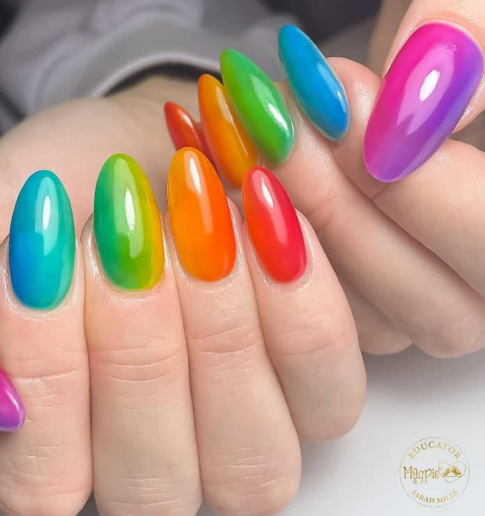 A closeup of a woman's long almond shaped nails with a flawless rainbow ombre effect