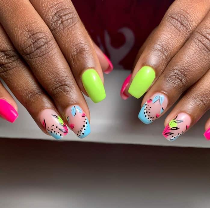 A closeup of a woman's long nails with nude, bright green and pink nail polish that has pastel blue sideway French tips, topped with black dots, and decorated with delicate leaves and stems on the side on nude nails 