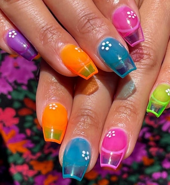 A closeup of a woman's short coffin nails with a vibrant base in purple, orange, blue, pink, and green that has floral art near the cuticles
