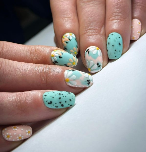 a woman's hand with pastel blue and pink nails with daisy flowers design
