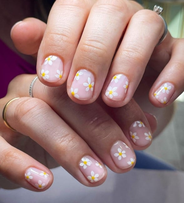 a woman's nails with translucent base and little daisies design