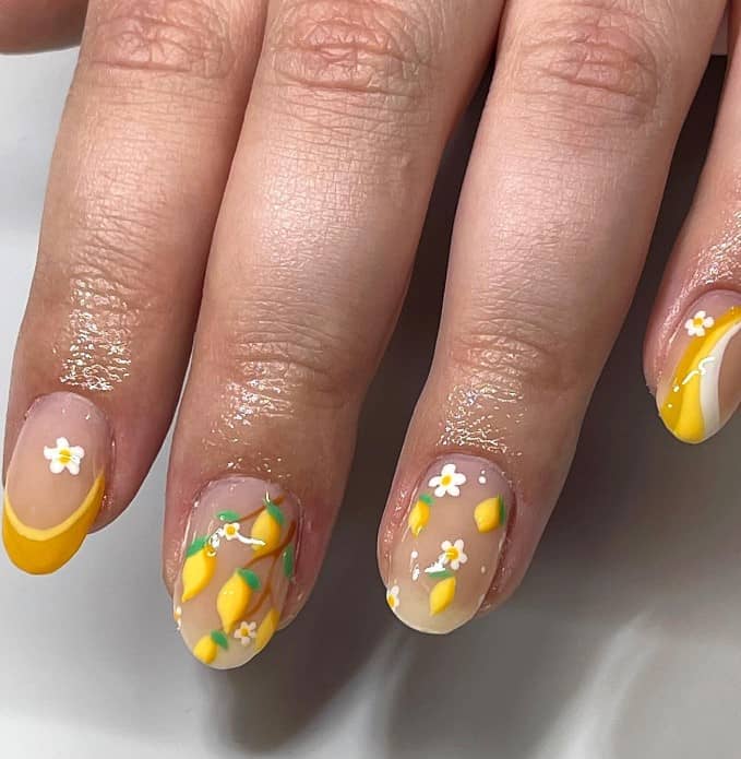 A closeup of a woman's fingernails with a nude nail polish base that has lemon yellow French tips, yellow and white streaks, and lemon fruits and flower