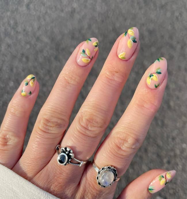 A woman's fingernails with a nude nail polish base that has lemons on branches nail designs