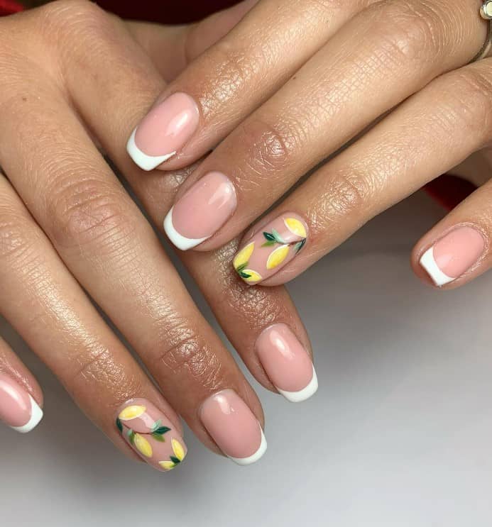 A closeup of a woman's fingernails with a nude nail polish base that has classic French tip design and lemons hanging from the branches 