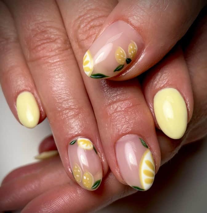 A closeup of a woman's fingernails with a nude and yellow nail polish base that has lemons on the tips, sides, and cuticles nail designs
