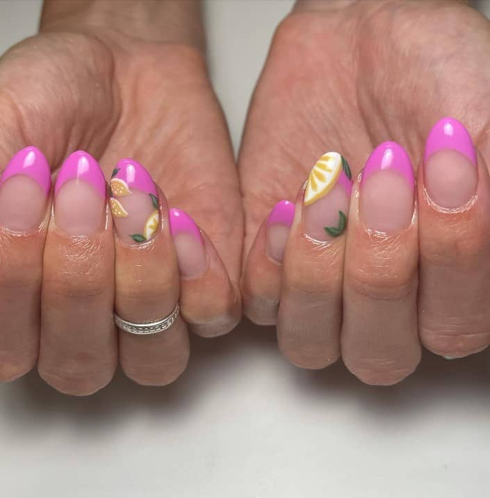 A closeup of a woman's fingernails with a nude nail polish base that has pink French tips and ripe lemons nail designs