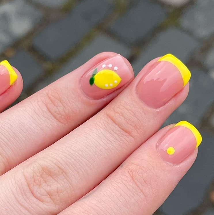 A closeup of a woman's fingernails with sheer champagne pink nail polish that has bright lemon yellow tips and tiny white polka dots on select nails 