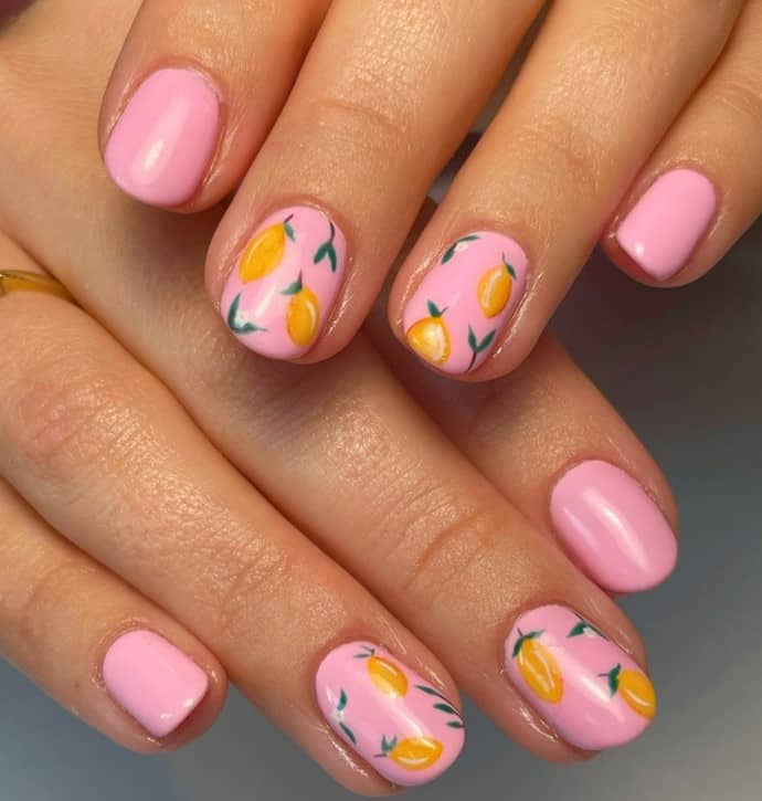 A closeup of a woman's fingernails with a pastel pink nail polish base that has lemon decorations on select nails