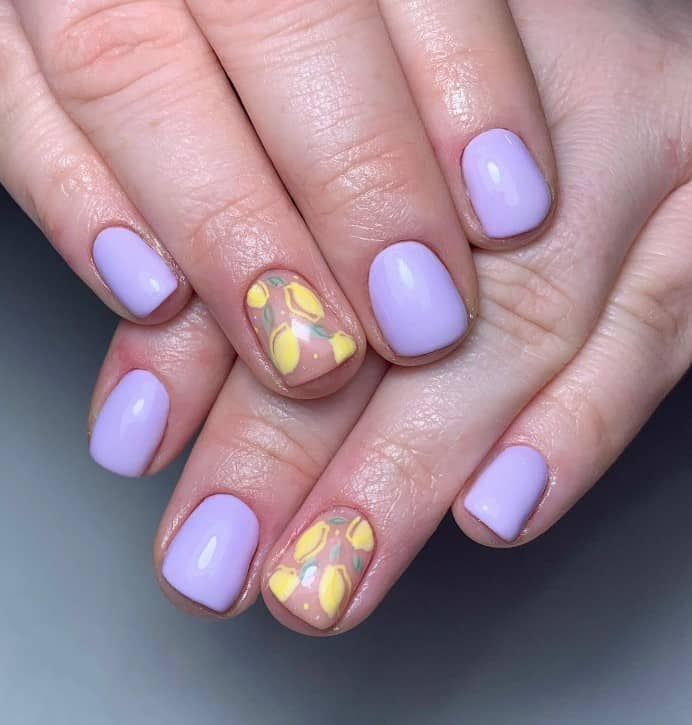 A closeup of a woman's fingernails with a lavender and nude nail polish that has lemon nail designs on nude nails 