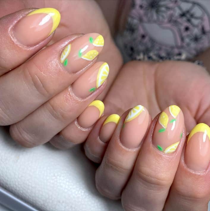 A closeup of a woman's fingernails with a nude nail polish base that has lemon yellow tips or lemon nail art