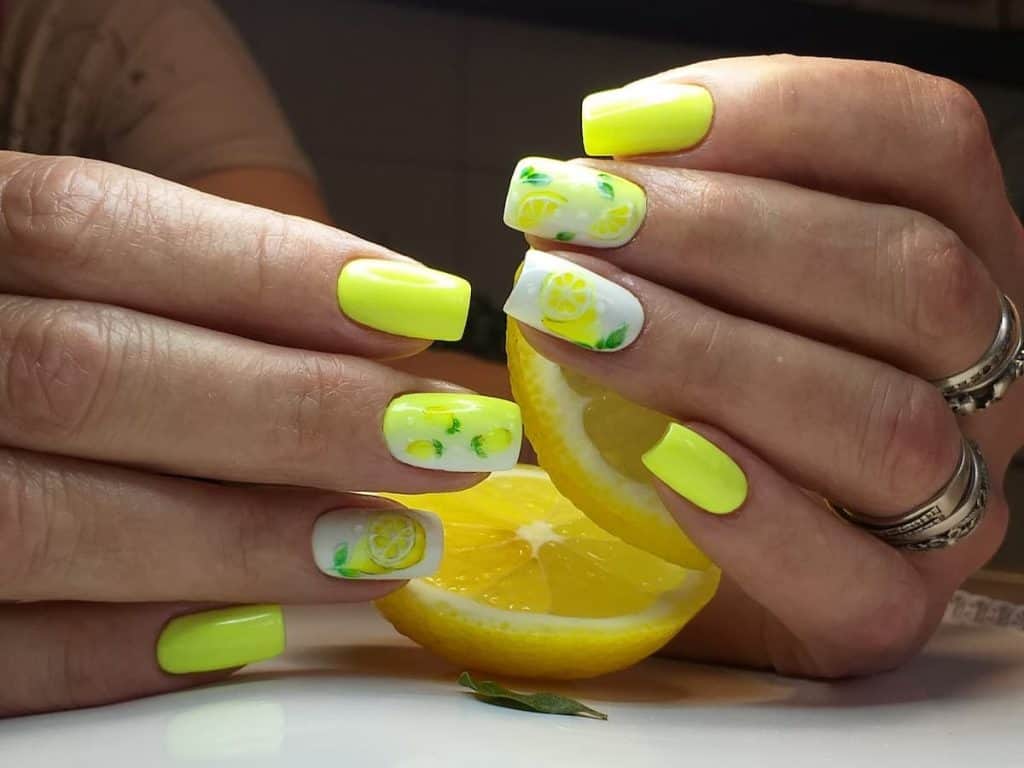 A closeup of a woman's fingernails with a combination of white and yellow nail polish that has lemon nail designs on white nails 