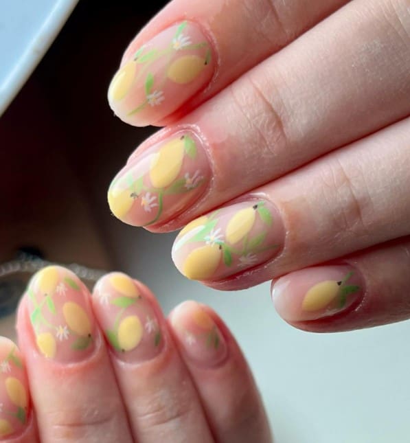 A closeup of a woman's fingernails with a nude nail polish base that has lemons and blossoming lemon flower nail designs