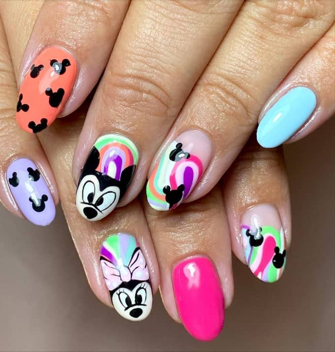 A closeup of a woman's fingernails with pink, peach, and blue nails that has kaleidoscopic Minnie and Mickey nail designs and Mickey silhouettes on select nails