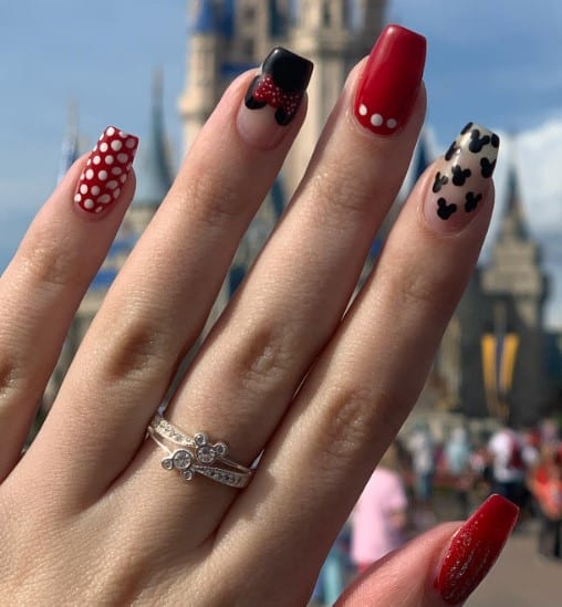 A woman's fingernails with nude and red glitter nails that has Minnie Mouse French tips and white polka dots on red nails 