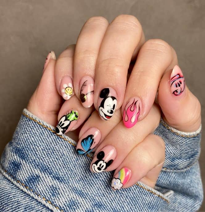 A closeup of a woman's fingernails with nude nail polish base that has Mickey Mouse art, butterflies, flowers, and rainbows nail designs