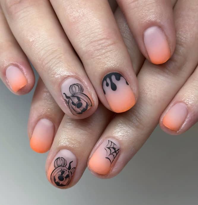 A closeup of a woman's fingernails with peach ombre nails that has Mickey-o’-lantern art and Halloween-inspired designs