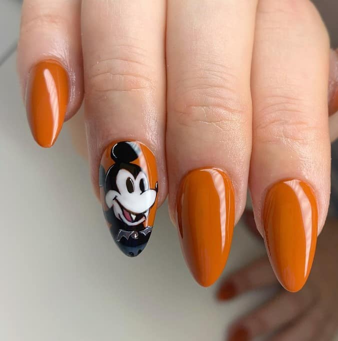 A woman's long almond-shaped fingernails with caramel brown nail polish that has Mickey Mouse art on select nails