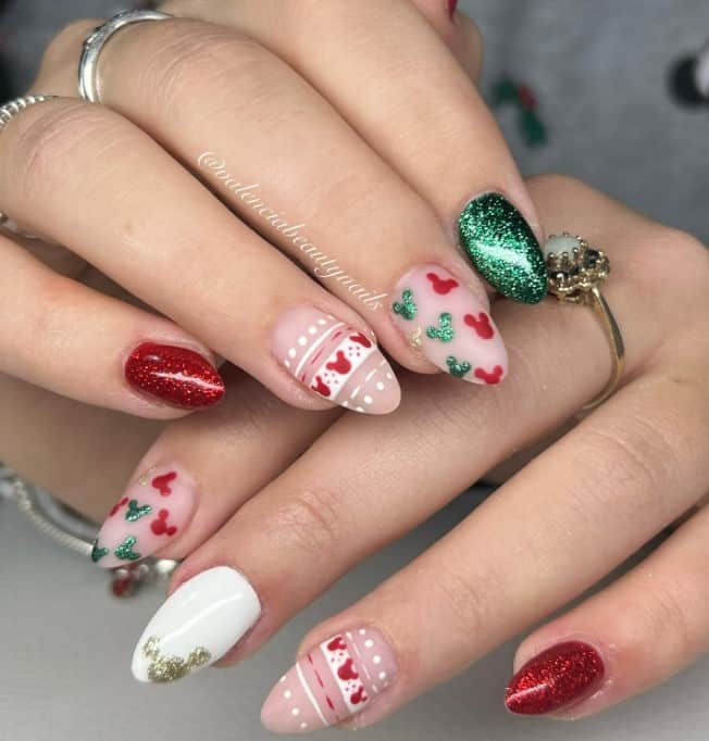 A closeup of a woman's fingernails with red and green glitter nails, a frosty white nails that has a glittery Mickey silhouette, and red and green glitter Mickey silhouettes