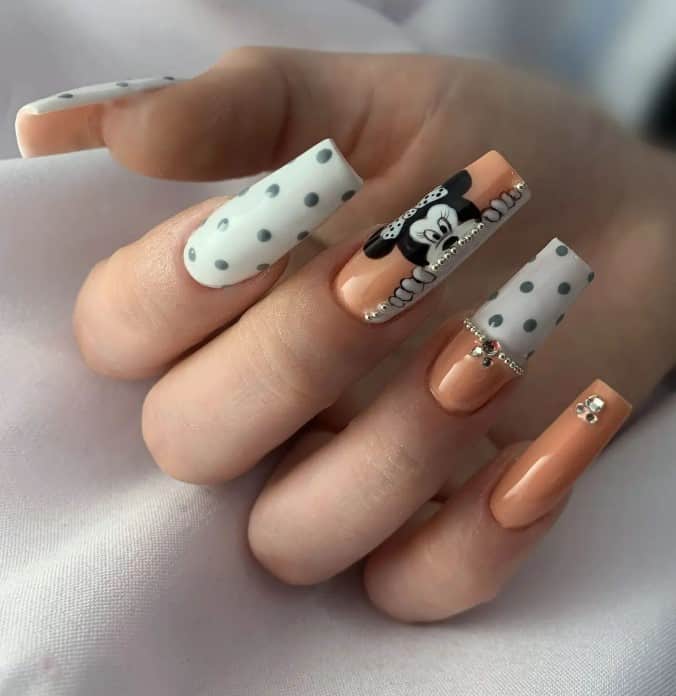 A woman's fingernails with white, black, and beige nails that has polka dots and jewels and peeping Minnie Mouse
