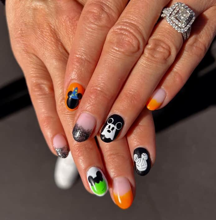 A woman's fingernails with nude, orange and black nail polish base that has Mickey Mouse silhouette, a green-and-black silhouette, a mummified one, and one with a wizard hat