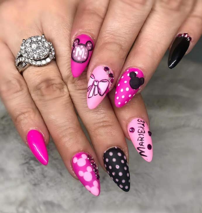A closeup of a woman's fingernails with pink and black nails that has Minnie and Mickey Mouse nails, white polka dots, Mickey silhouettes, and rhinestone cuffs
