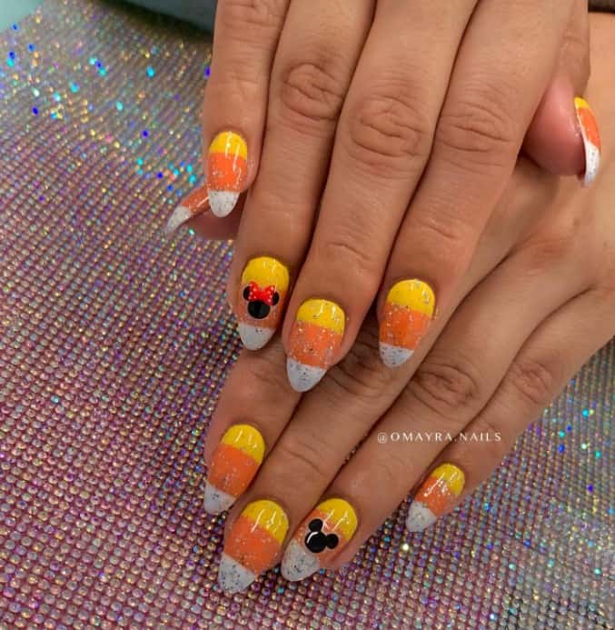 A woman's fingernails with yellow, orange, and white stripes that has silver glitter along with Minnie and Mickey Mouse art
