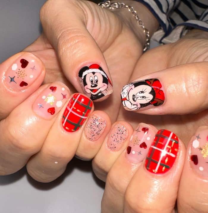 A closeup of a woman's fingernails with nails in Mickey and Minnie in Santa suits, red plaid designs, silver glitter, and red hearts and snowflakes nail designs