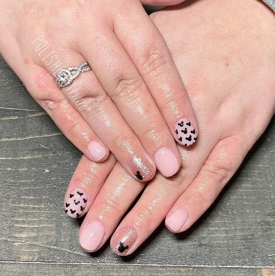 A woman's fingernails with a pinkish-nude and glittery pink nail polish that has a Mickey silhouette pattern and Mickey Mouse nail art on pink glitter nails