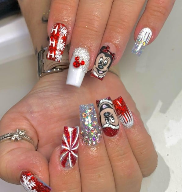 A woman's fingernails with red and white glitter that has red Mickey-shaped rhinestones, large gems on glitter nails, frost-like designs on the cuticles, and white snowflakes
