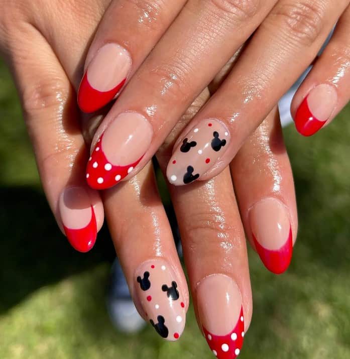 A closeup of a woman's red French tips fingernails with polka dots that has nude accent nails that sport Mickey Mouse silhouettes