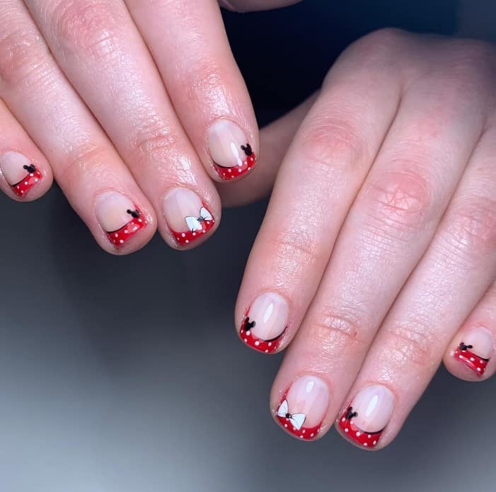 A closeup of a woman's fingernails with red and white polka dot Frenchies that has Mickey Mouse's ears and Minnie Mouse’s white ribbon