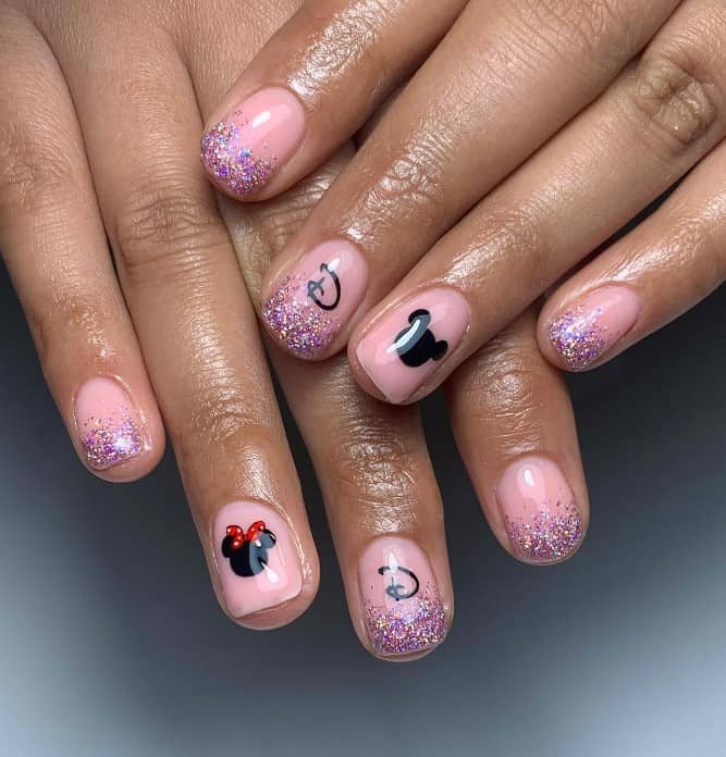 A closeup of a woman's fingernails with Mickey and Minnie Mouse silhouettes and Disney logos on light pink nails that has purple glitter ombre tips