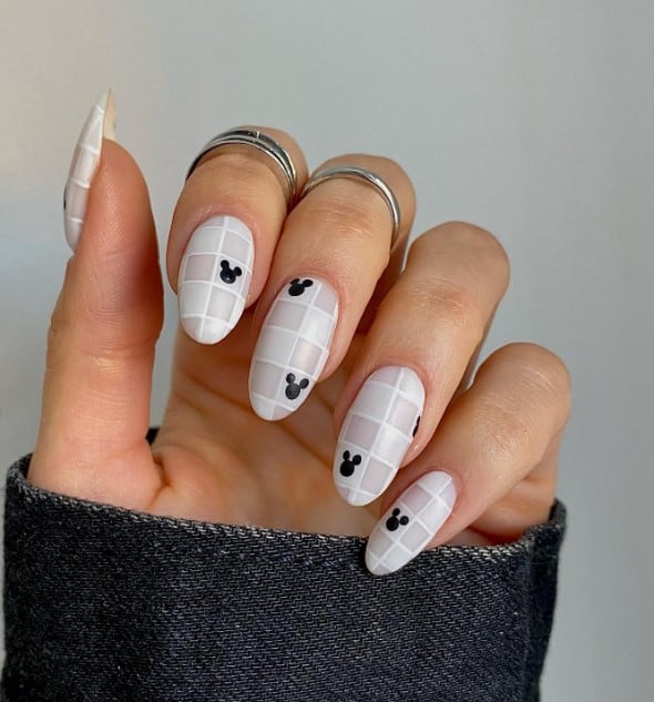 A closeup of a woman's fingernails with gorgeous white checkered nails that has Mickey Mouse silhouette accents