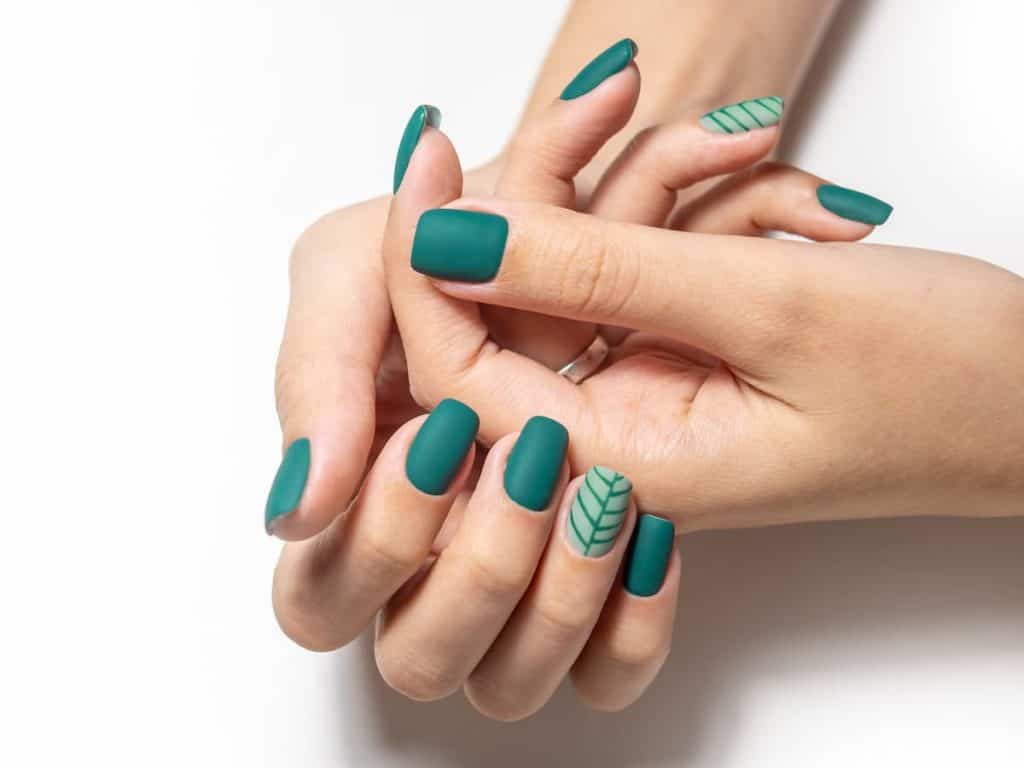 A woman's hands with green manicured nails on top of a a white background