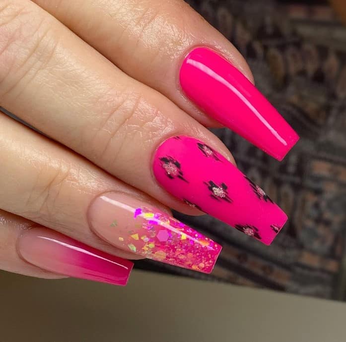 A closeup of a woman's fingernails with a mix of nude and hot pink nail polish base that ahs solid and ombré designs, leopard print and confetti glitter