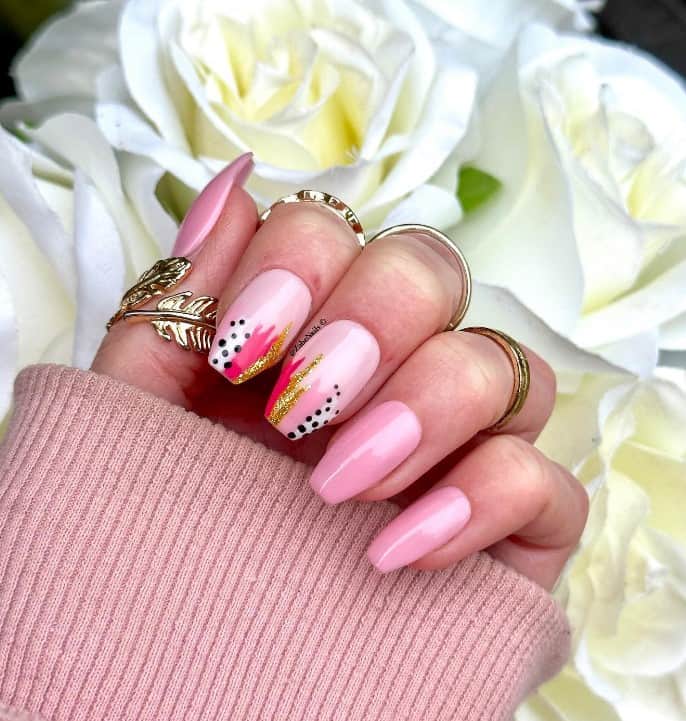 A woman's fingernails with a baby pink polish that has abstract art on the tips, polka dots and splatters in gold nail designs