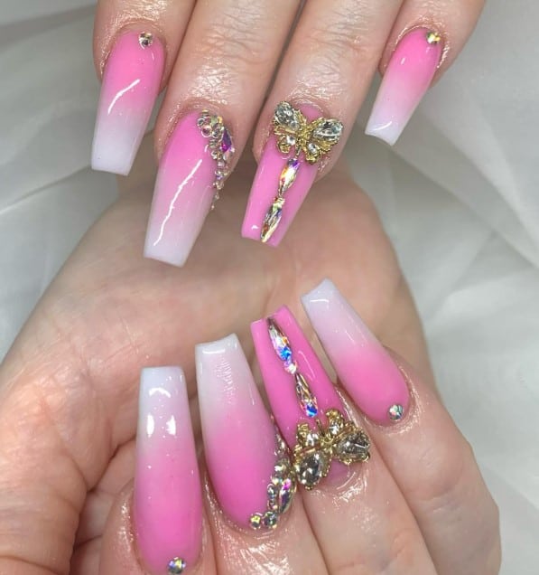 A closeup of a woman's fingernails with a white-and-pink coffin nails that has butterflies and rhinestones designs