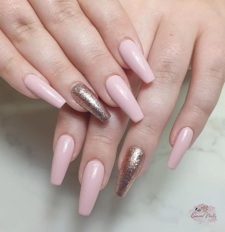 A closeup of a woman's fingernails with light pink nails that has one nail with gold glitter 