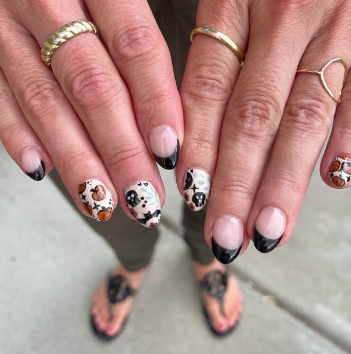 A closeup of a woman's fingernails with a nude and solid white nail polish base that has black French tips to select nails, black skulls and dark brown pumpkins