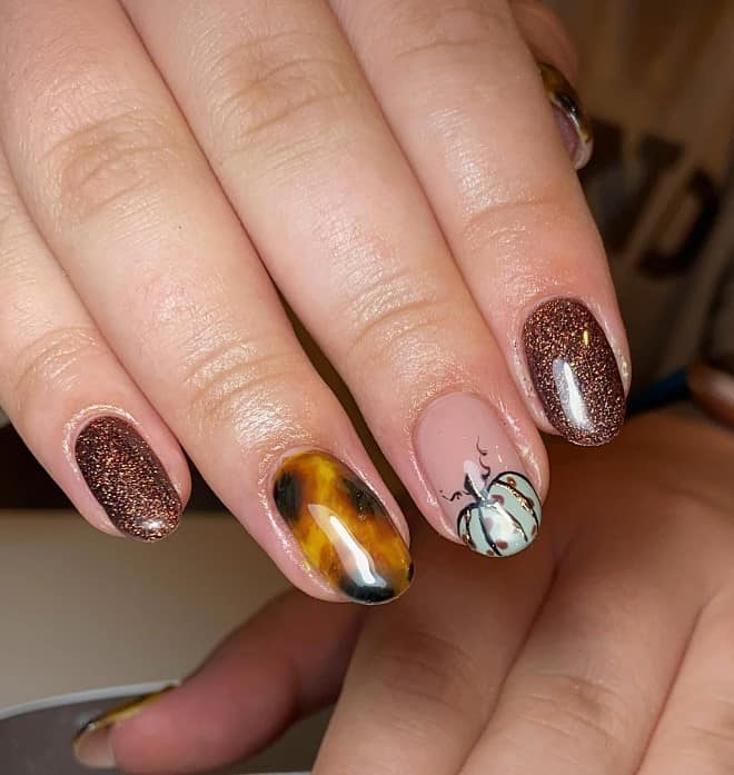 A closeup of a woman's fingernails with a brown and tortoiseshell nails that has white pumpkin on the accent nail highlights