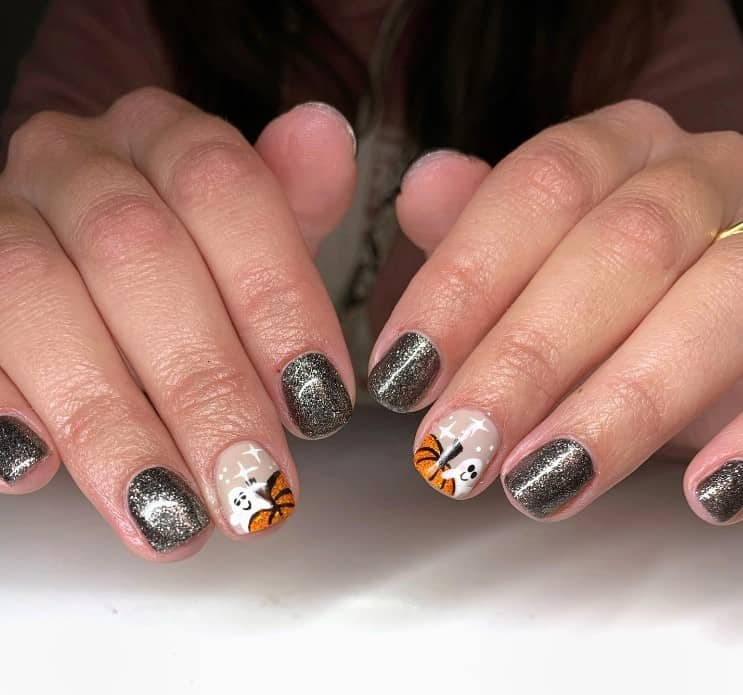 A closeup of a woman's fingernails with a nude and black nail polish in glitter finish that has ghosts and pumpkins nail designs on nude nails