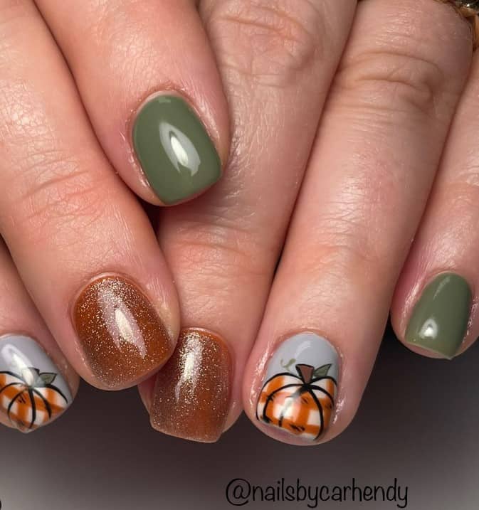 A closeup of a woman's fingernails with dark green, brown, and gray nail polish base that has a pumpkin with a checkered pattern on top of the gray nail