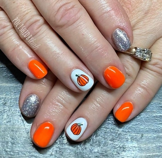 A closeup of a woman's fingernails with a white and orange nail polish base that has little pumpkin to the white nails