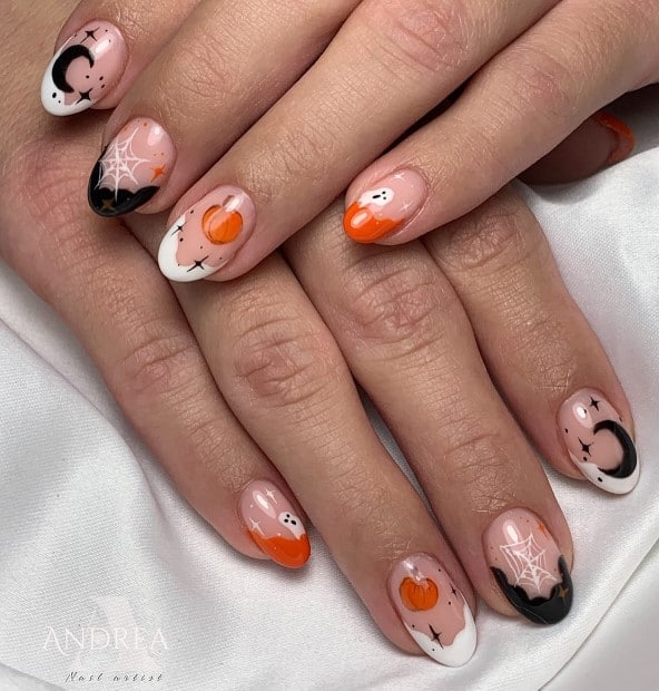 A closeup of a woman's fingernails with a nude nail polish base that has stars, moons, pumpkins, ghosts, and spiderwebs in black, orange, and white